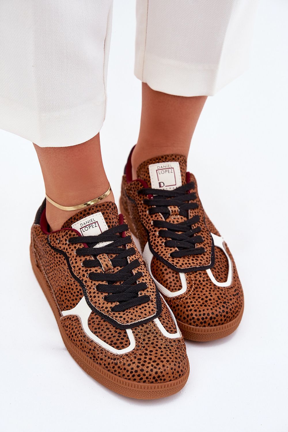 Leopard print sneakers with black laces, worn by a person in white pants, showcasing casual style and urban fashion.
