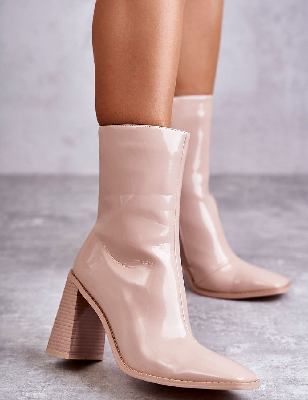 Woman wearing Lumirelle Glossflare Calf Silhouette boots with lacquer-finish and high stiletto heels on a textured floor.