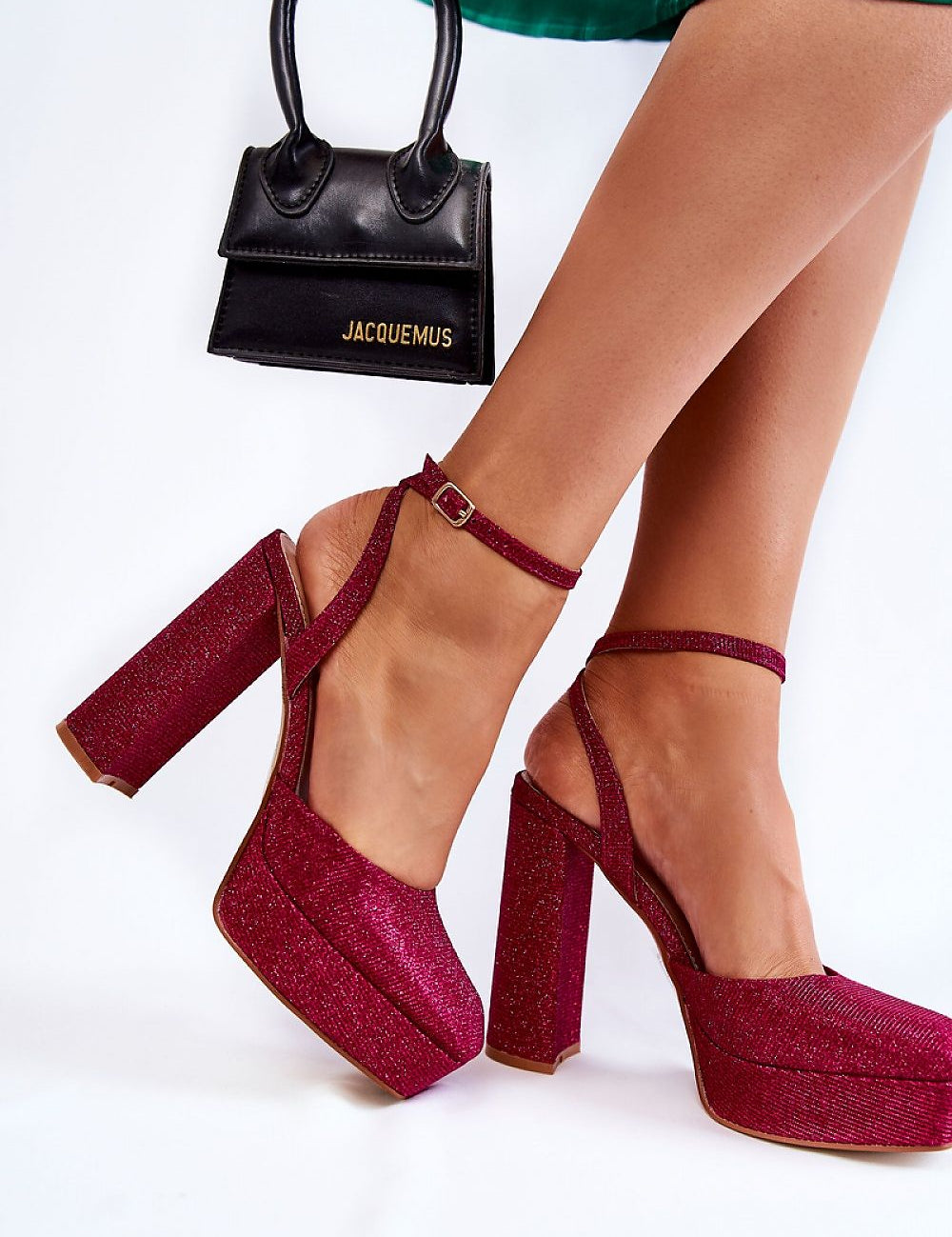 Woman wearing glittery red platform sandals with ankle strap, carrying a small black handbag, showcasing elegant evening footwear.