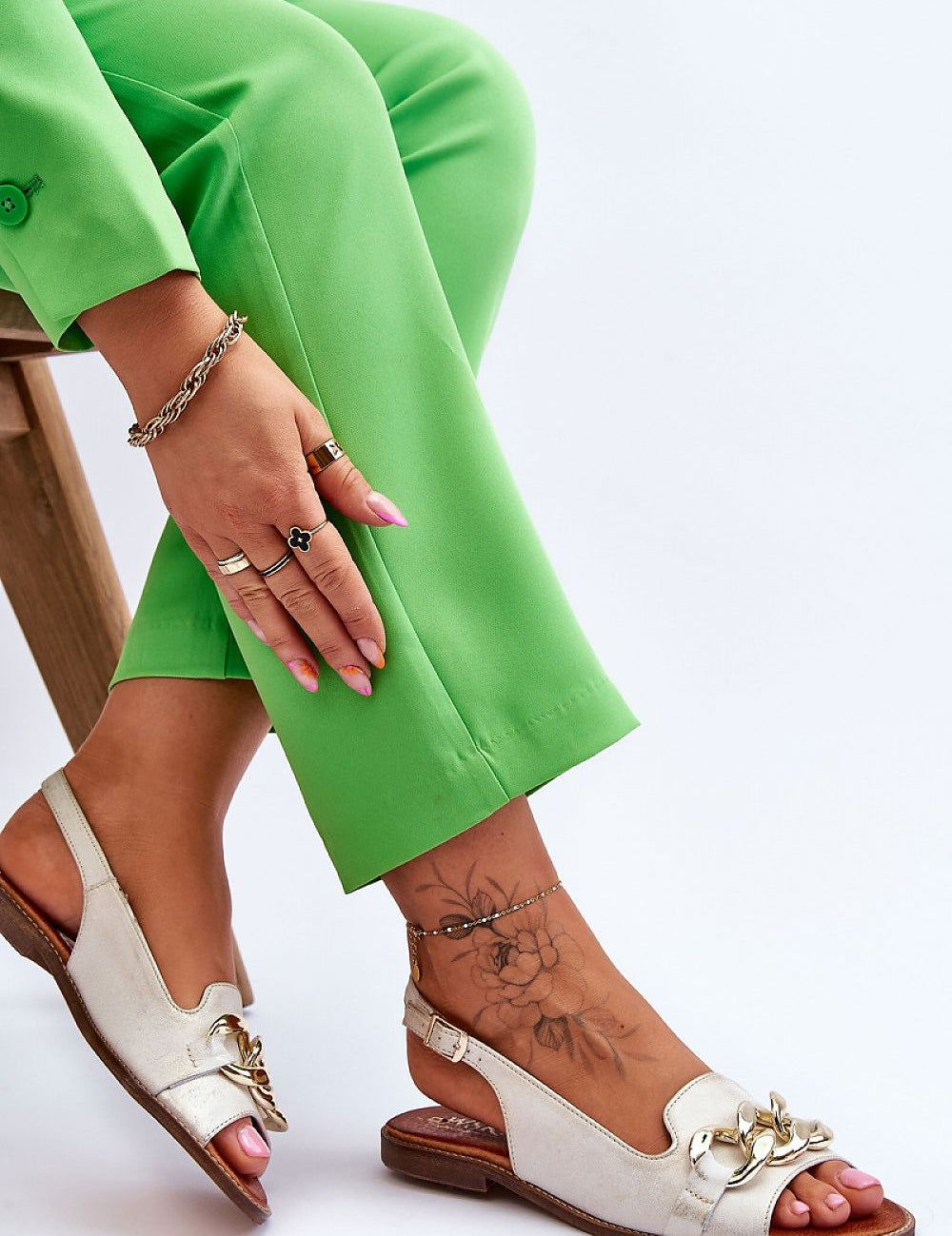 Woman wearing Chainlight Leather Flat Sandals with decorative chain detail, styled with green pants and accessorized with jewelry.