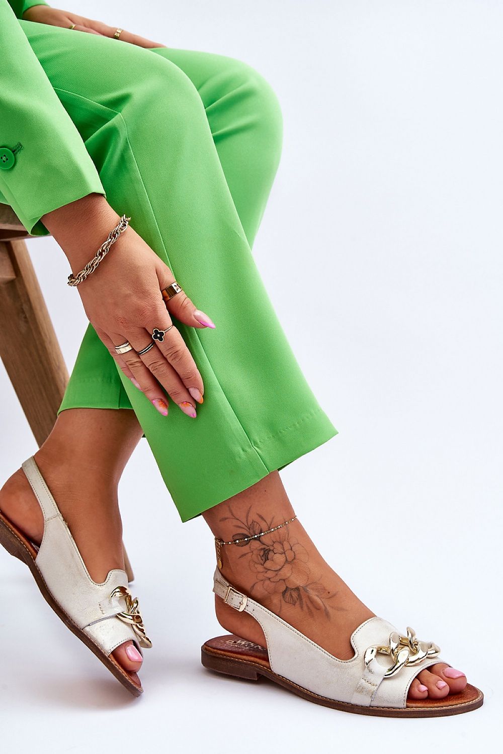 Woman wearing Dorellia Leather Flat Sandals with chain detail, paired with green pants.