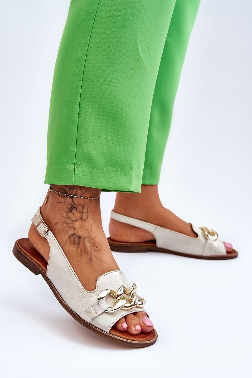 Woman wearing Chainlight Leather Flat Sandals with chain detail, styled with green pants, showcasing modern and stylish summer footwear.