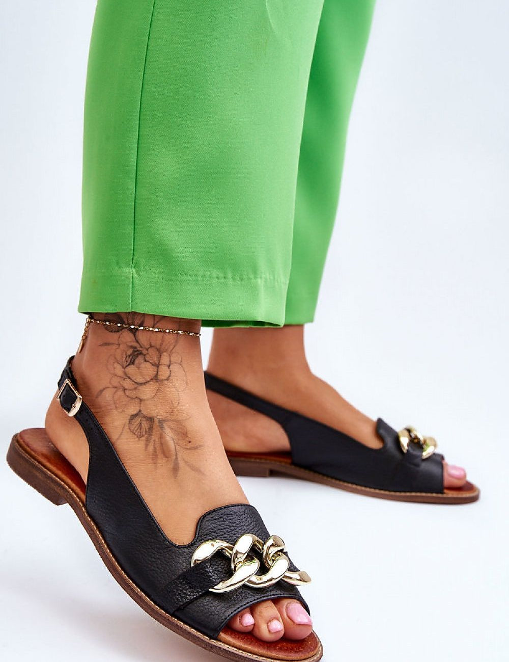 Woman wearing Valaro Chain Accent Leather Sandals with decorative front strap and green pants.