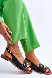 Woman wearing Valaro Chain Accent Leather Sandals with green pants, showing decorative chain detail and adjustable buckle strap.