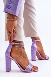 Woman wearing purple satin heel sandals with ankle strap and rounded open toe, styled with chic outfit for formal occasion.