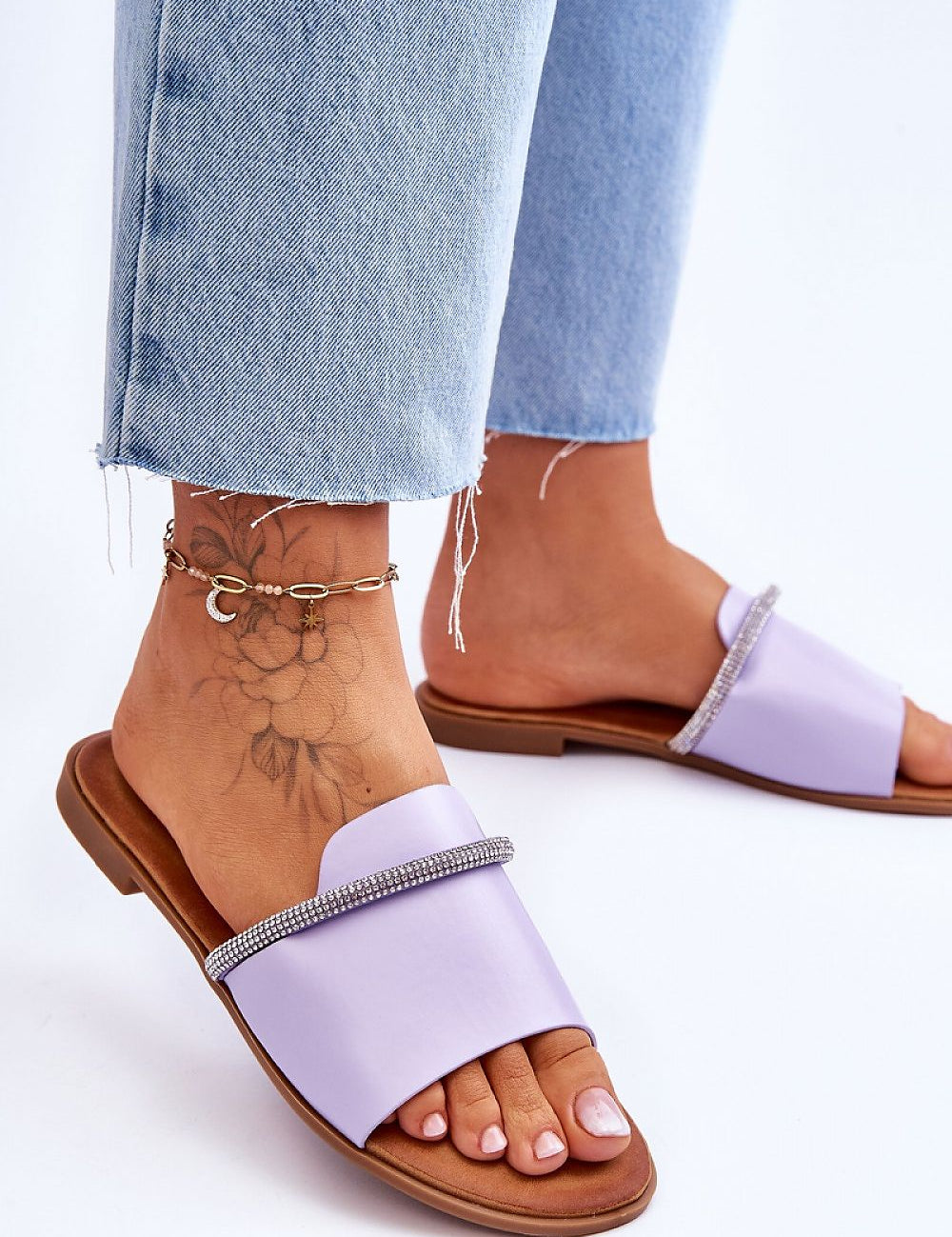 Woman wearing purple flat rhinestone flip-flops with denim jeans, showcasing minimalist design and casual style.