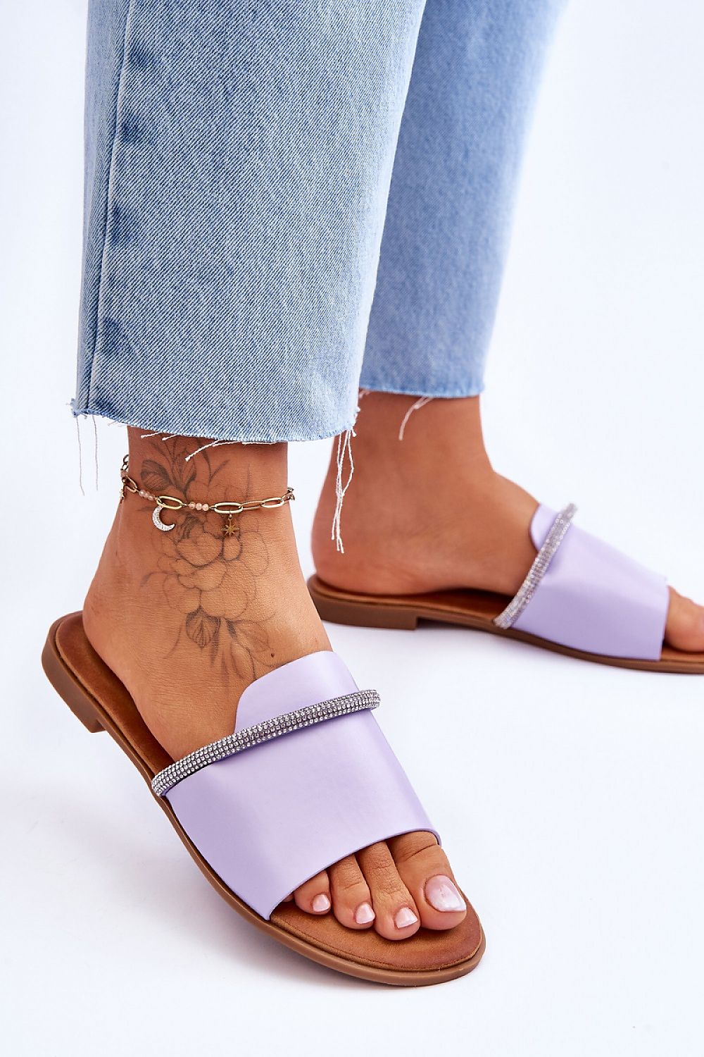Woman wearing purple flat rhinestone flip-flops with denim jeans, showcasing minimalist design and casual style.