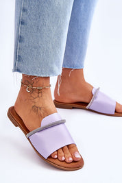 Woman wearing purple flat rhinestone flip-flops with denim jeans, showcasing minimalist design and casual style.