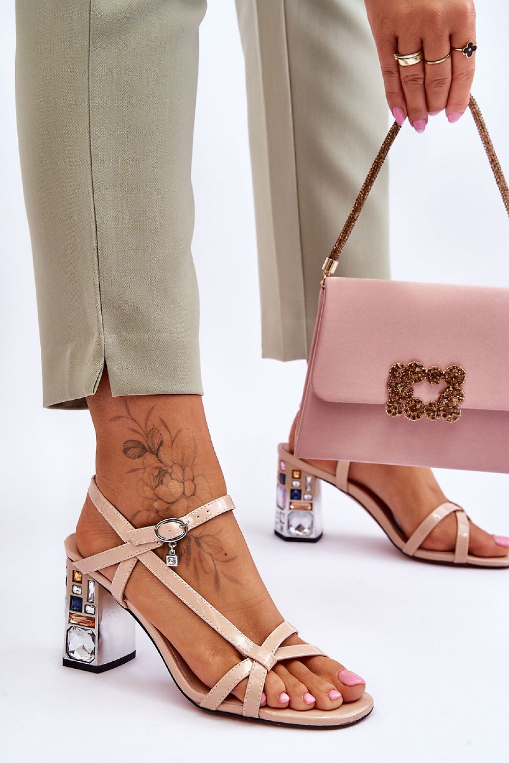 Woman wearing Carinea High Heel Sandals with eco leather straps and jeweled stiletto, holding a pink handbag with floral design.