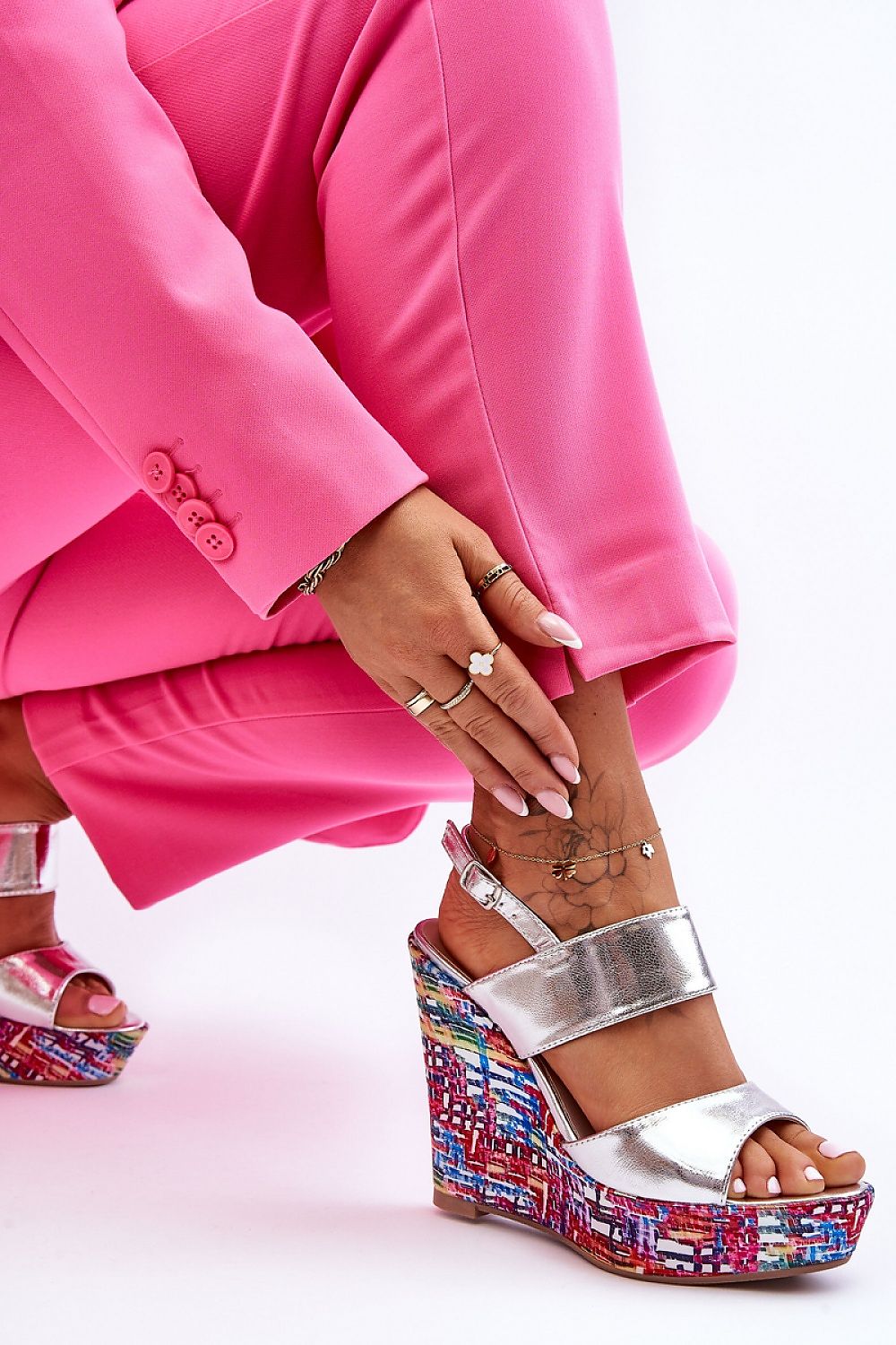 Woman in pink suit wearing Sarvella high-heel fusion sandals with metallic straps and colorful platform on tattooed ankle.