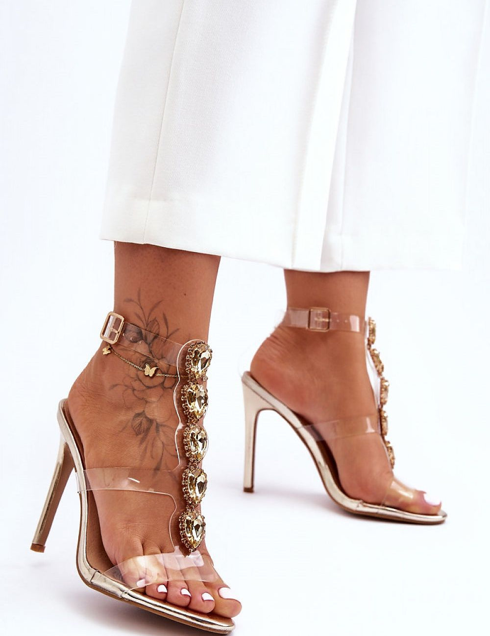 Woman wearing Astrielle High-Heel Crystal Sandals with rhinestone embellishments and transparent upper.