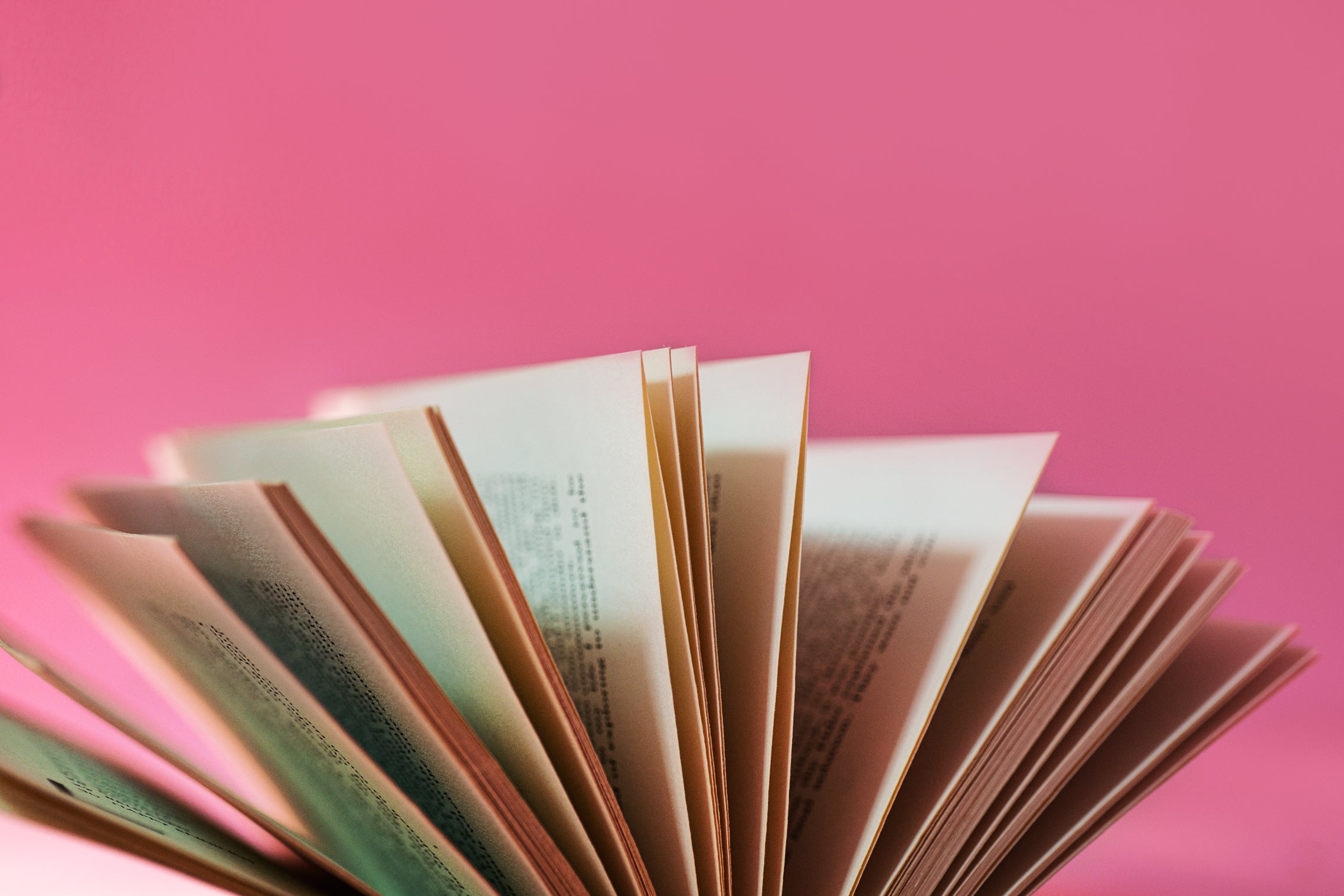 Open book with pages fanned out against a vibrant pink background, highlighting the written text and binding.