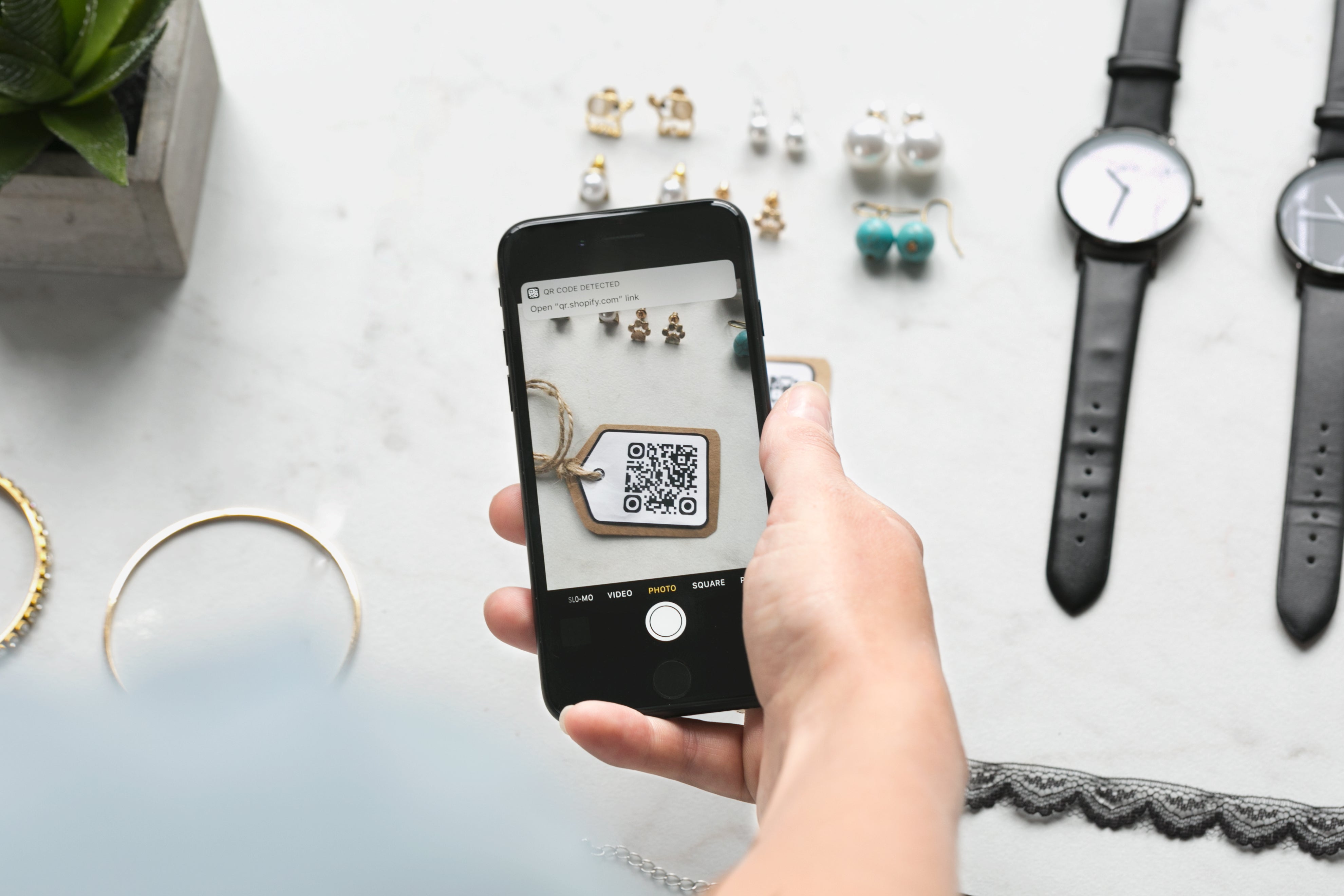 Person holding smartphone scanning QR code with jewelry and watches in the background
