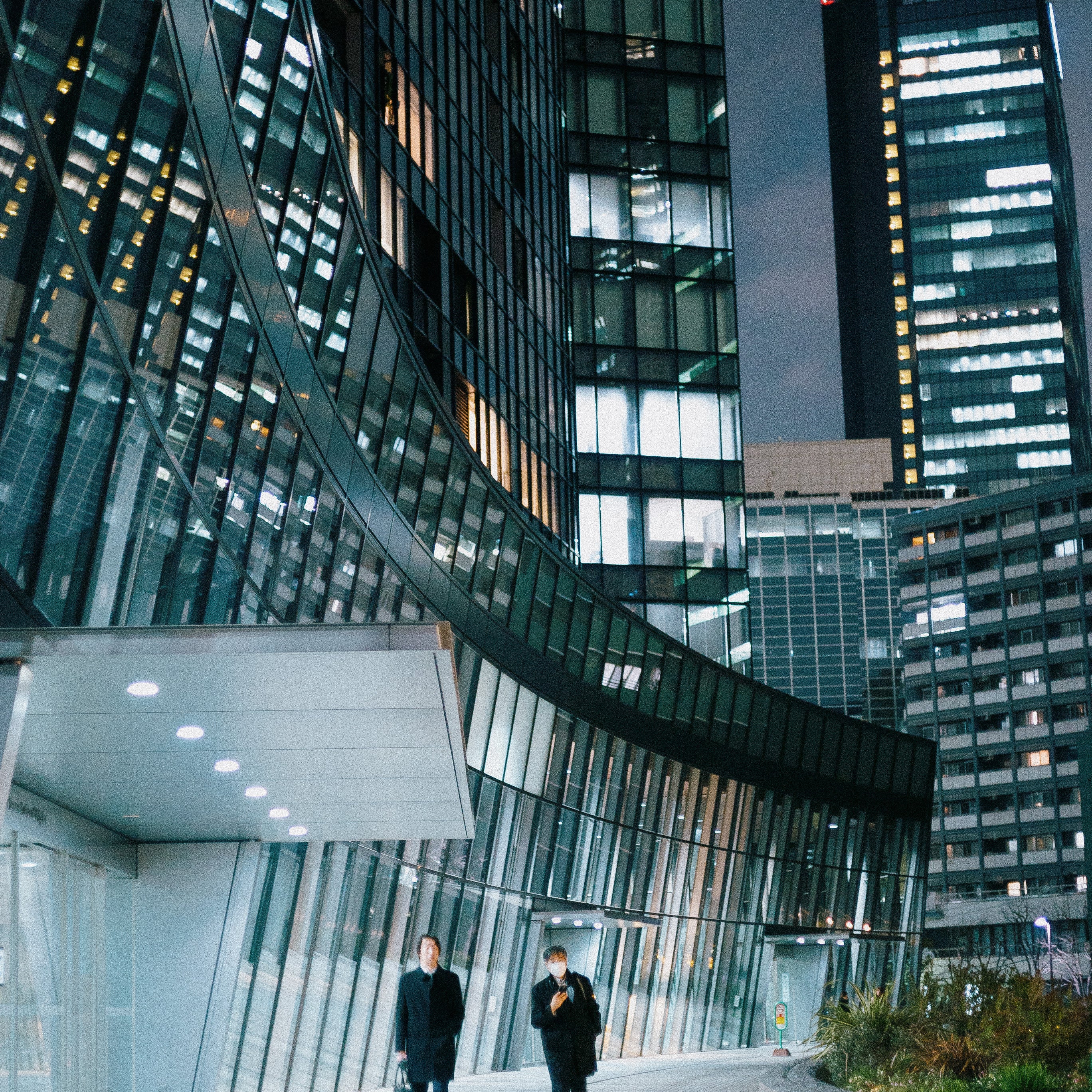 Two people walking outside modern glass skyscraper at night in a city downtown area.
